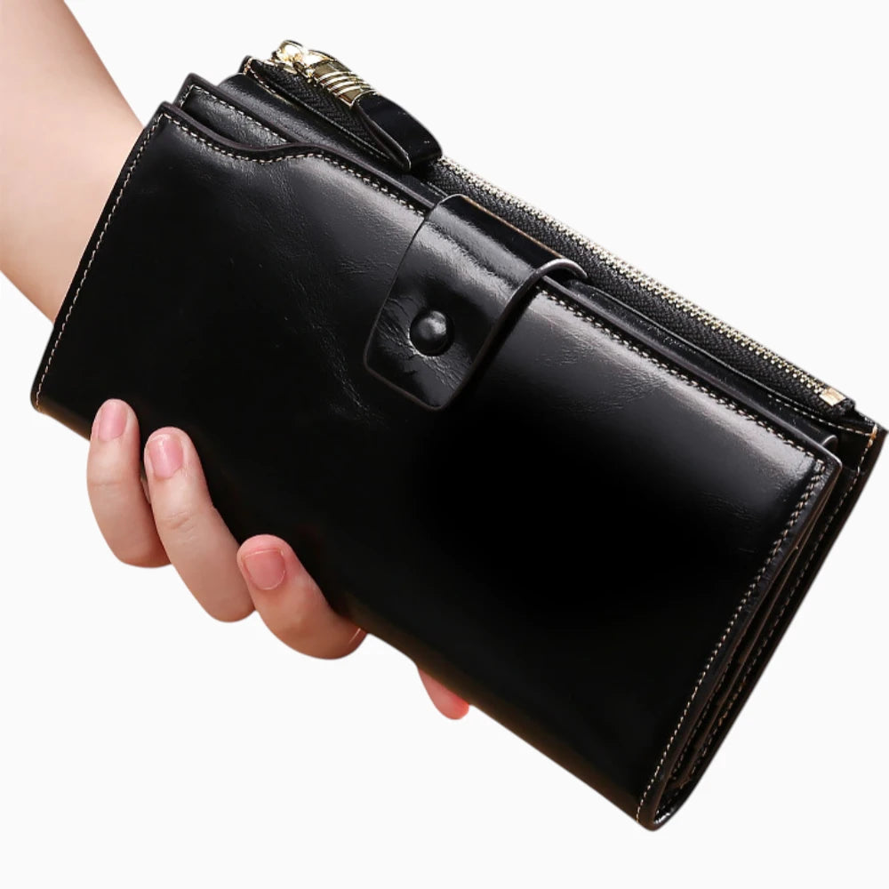 Portefeuille cuir noir femme avec bouton pression et fermeture zip tenu en main